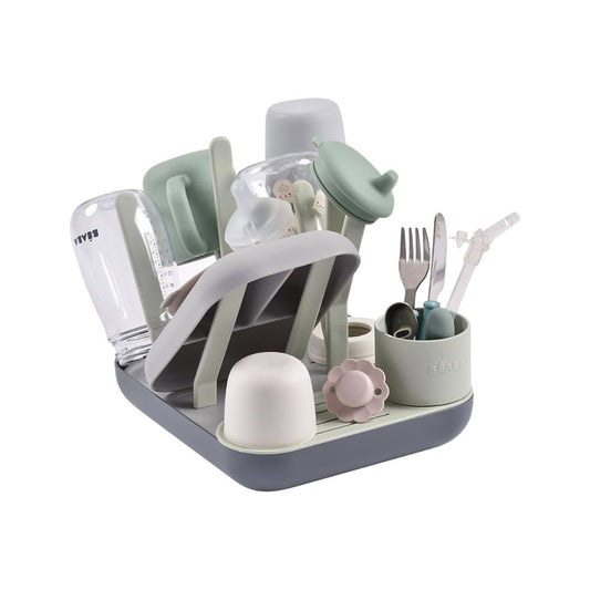 A Béaba bottle drying rack with various baby bottle parts and accessories neatly organized on it, featuring a space-saving design with multiple pegs of varying heights and shapes.
