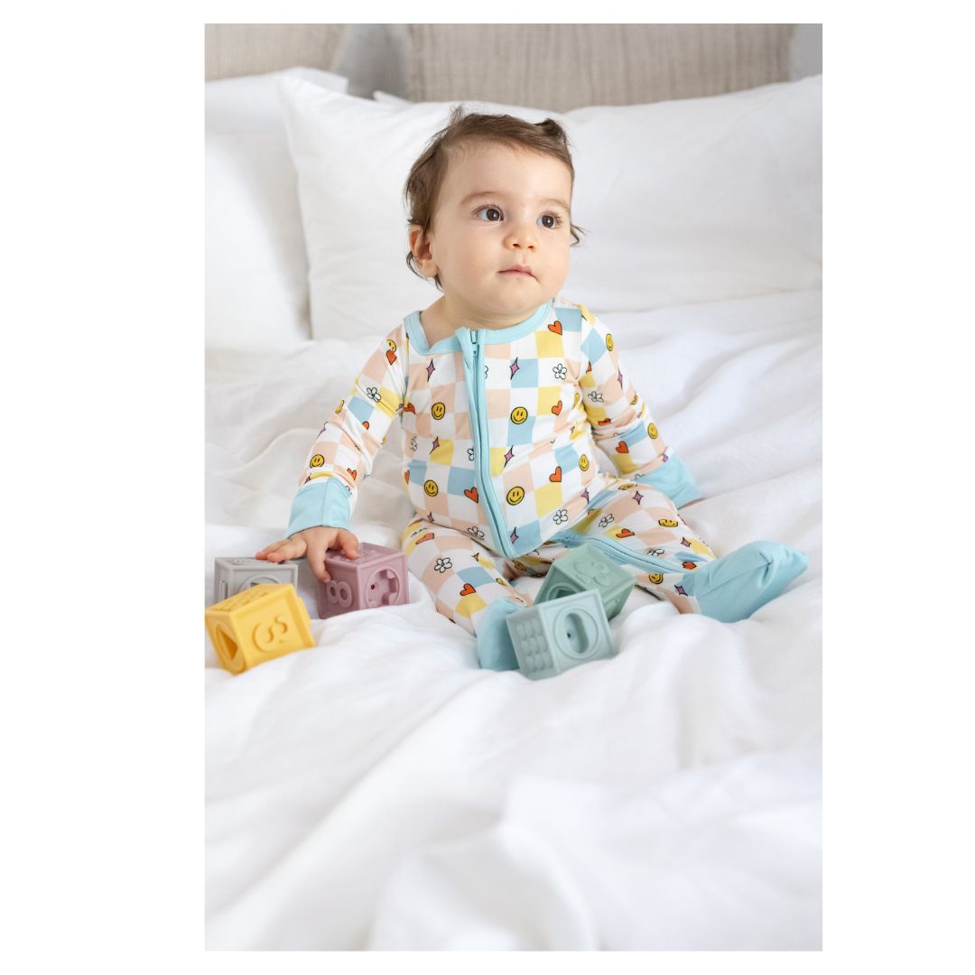 Baby sitting on a white blanket with colorful pajamas and toys.