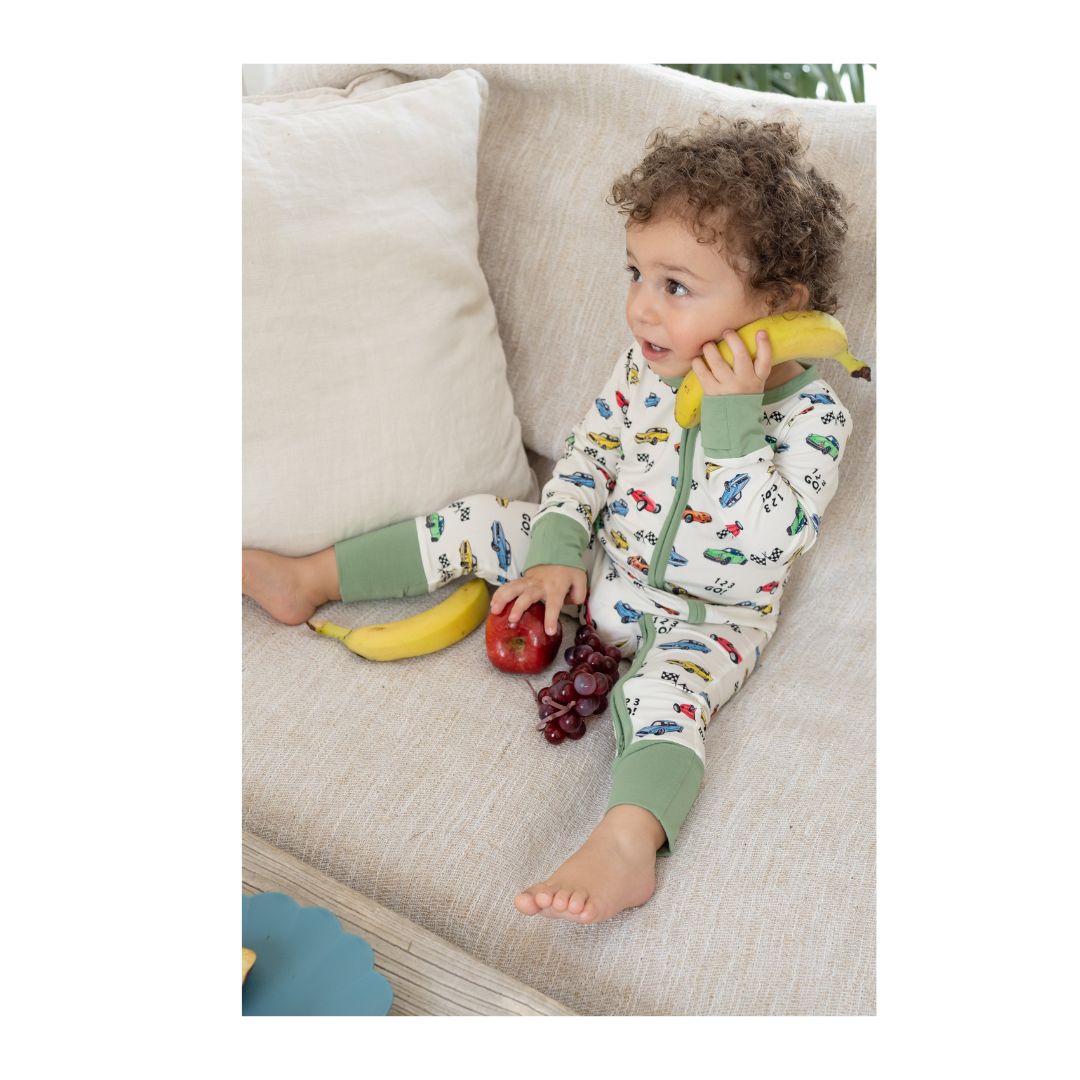 Child in pajamas holding a banana, sitting on a couch with fruits around