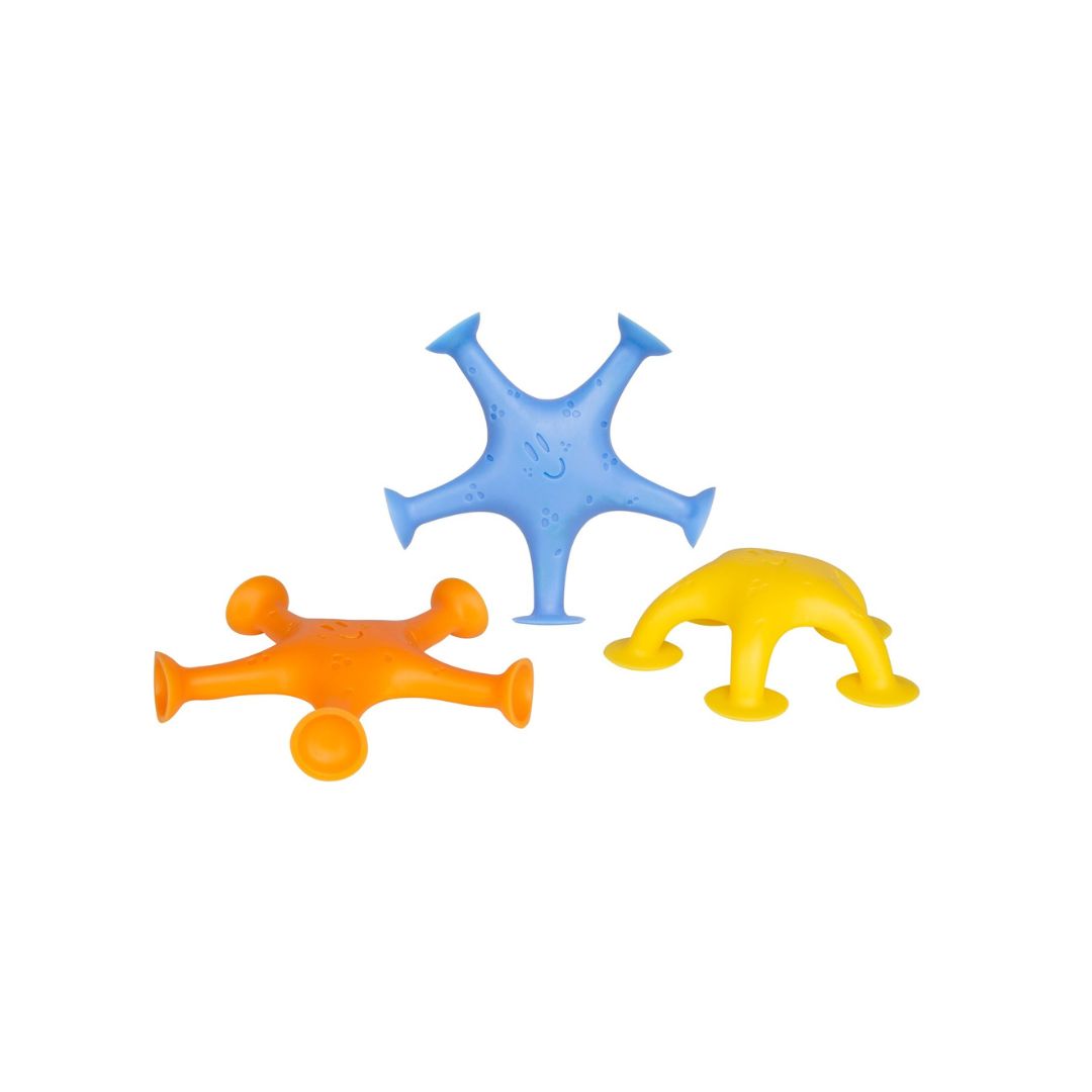 Set of three Ubbi Starfish bath toys in blue, orange, and yellow suctioned to a white bathtub wall.